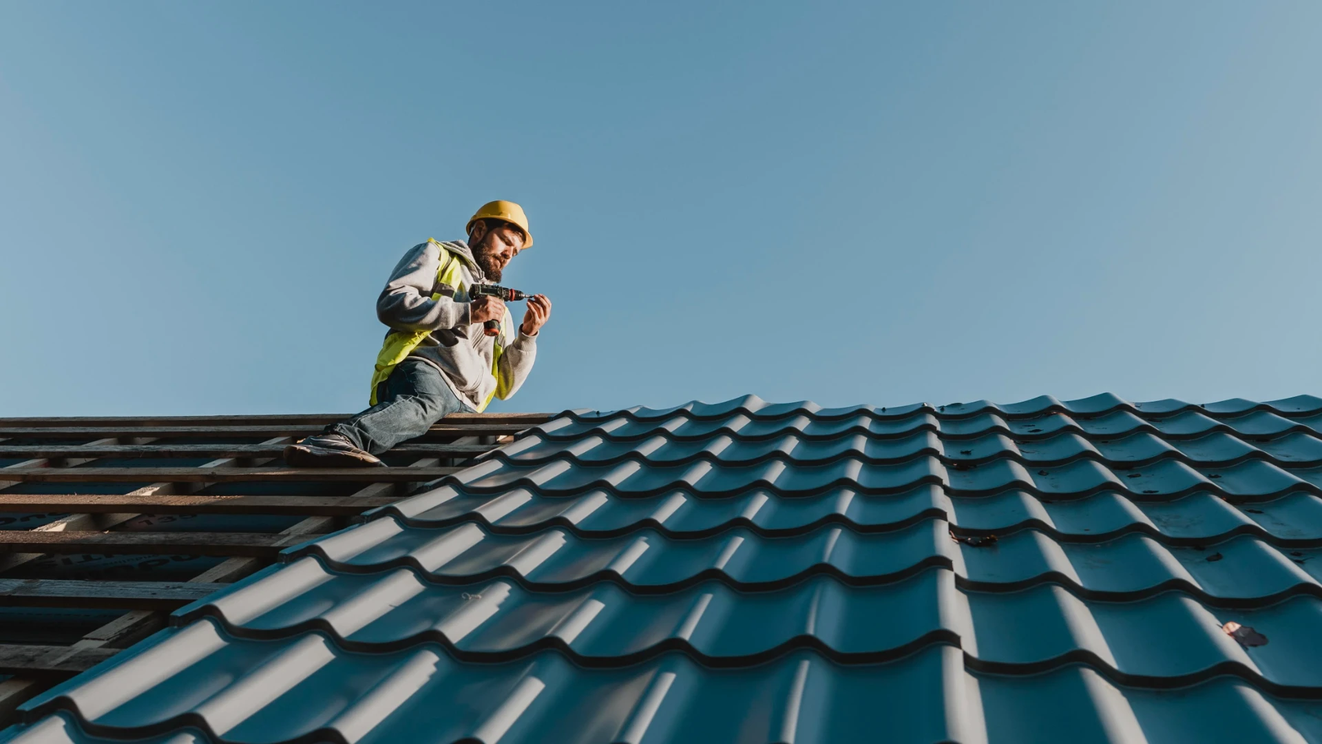 Roofer securing tiled roof sheets on a house against a clear sky
