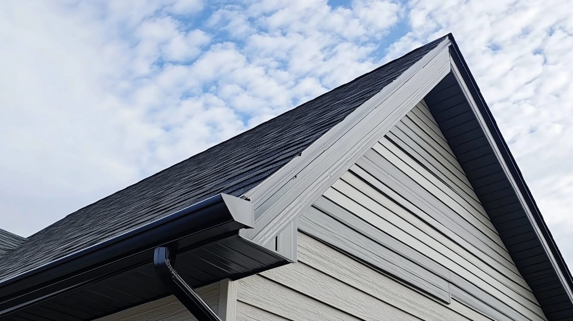 Gable end with new bargeboard, black gutter and downpipe against a cloudy sky