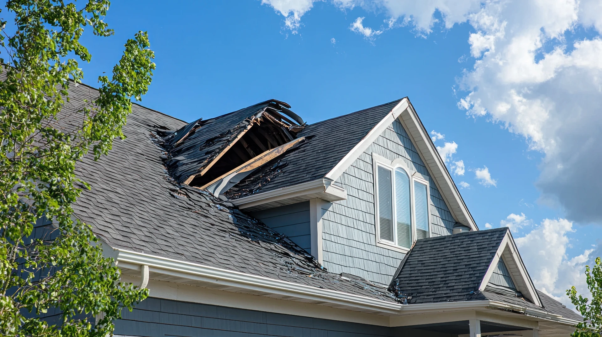 House roof torn open with broken shingles after a severe storm