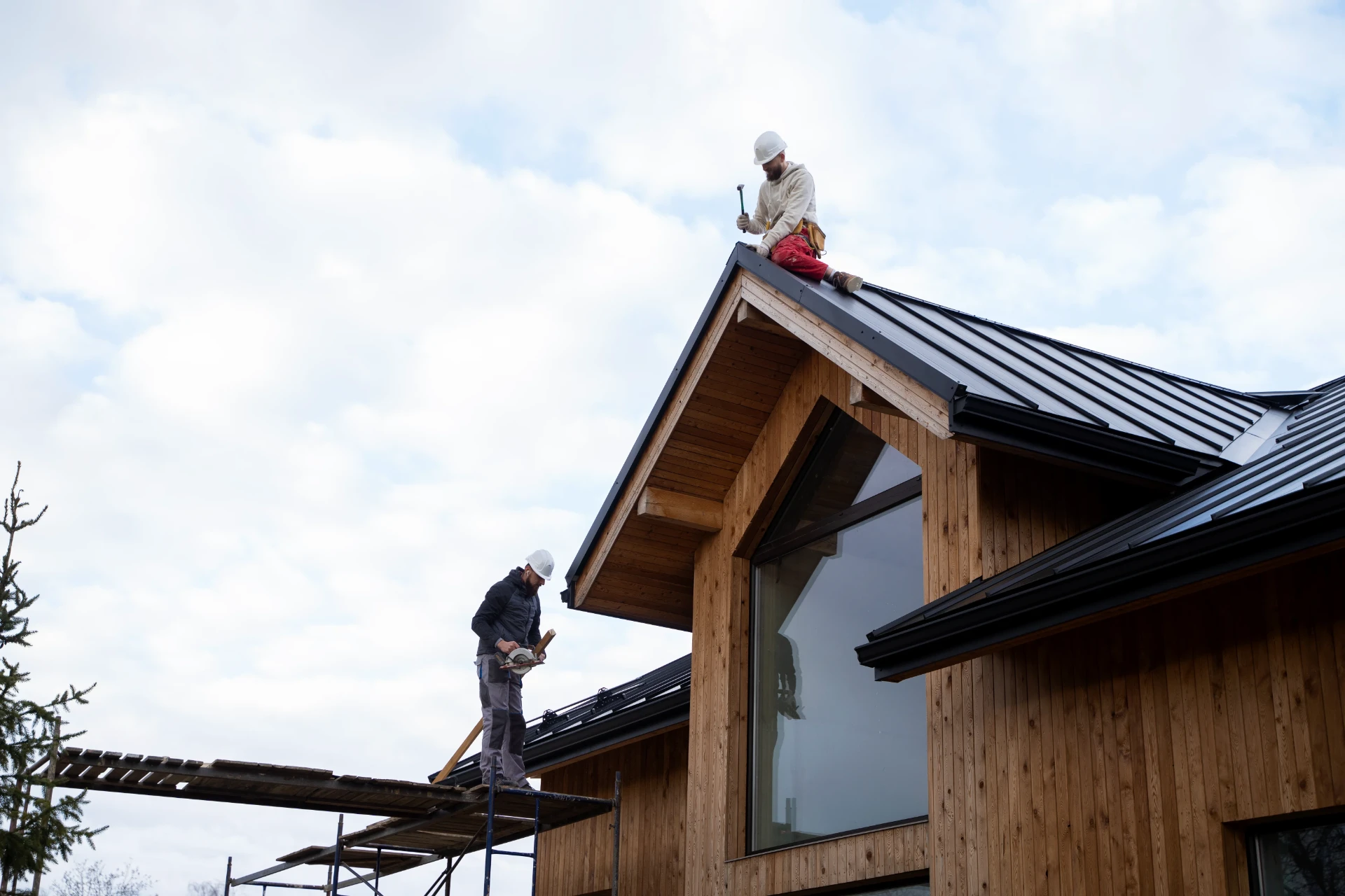 Two roofers working on a pitched standing-seam roof from scaffolding